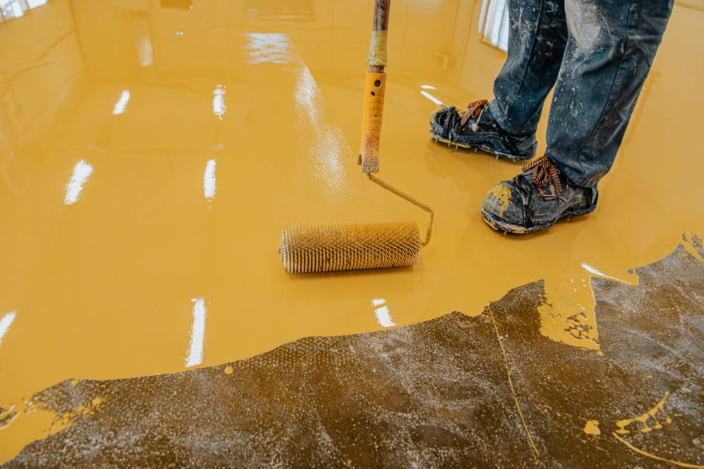 Worker, coating floor with self-leveling epoxy resin in industrial workshop.