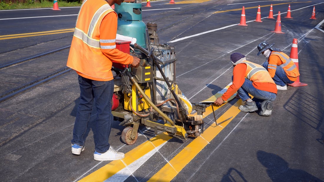 Road workers with thermoplastic spray marking machine painting traffic yellow lines on asphalt road